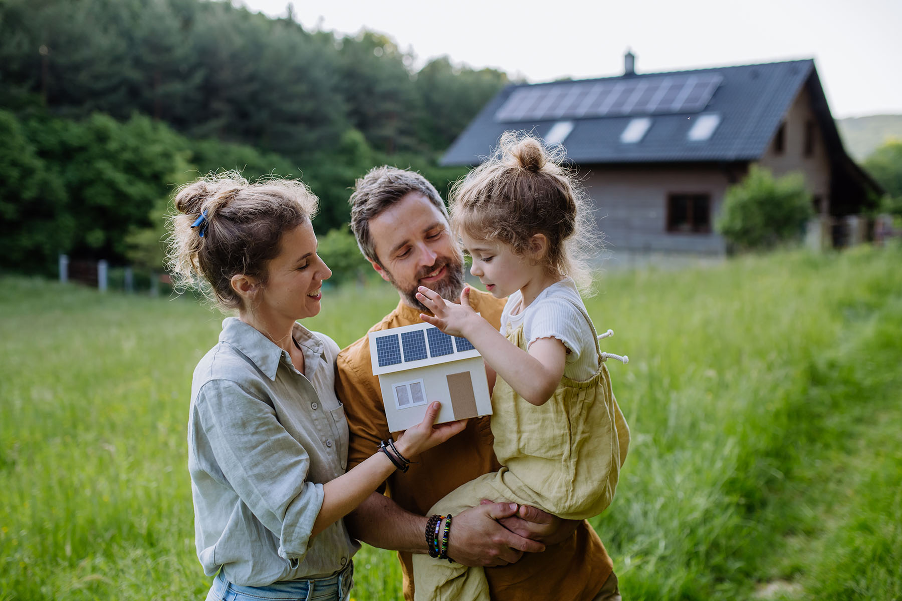 Happy family in front of their house with solar panels on the roof.
