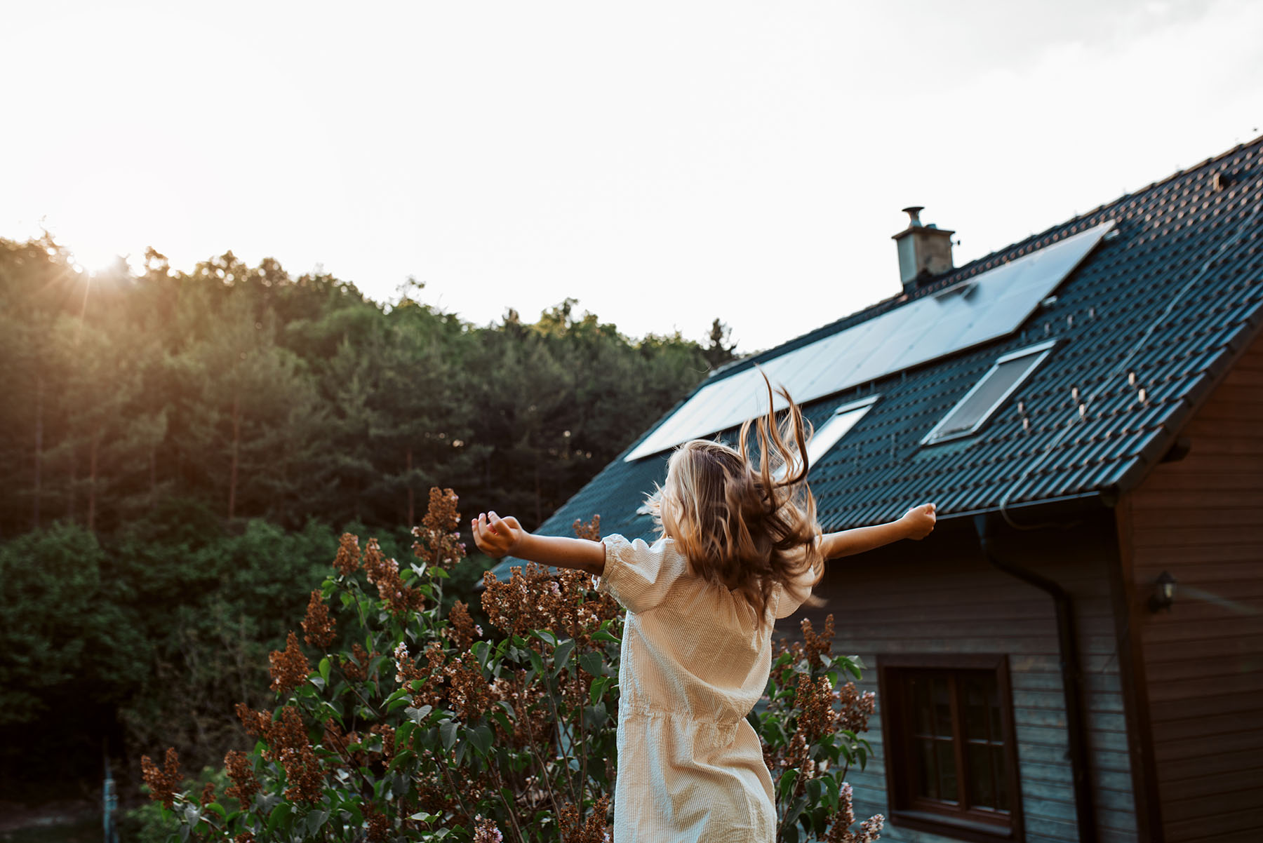 Little girl in front of house with solar panels on roof, jumping, dancing and having fun. Concept of renewable resources.